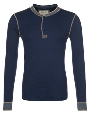 Chemise henley bleu marine à manches longues avec deux boutons, coutures contrastées et poignets gris sur un fond uni.