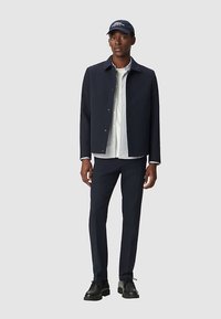 Granatowa kurtka zapinana na guziki z długimi rękawami, noszona na białej koszuli. Granatowe spodnie o dopasowanym kroju i czarne buty, do tego granatowa czapka.