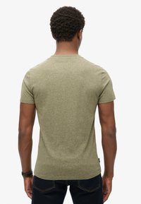 T-shirt fitted di colore verde oliva con maniche corte, scollatura rotonda e tessuto testurizzato. Abbinato a jeans scuri, visto da dietro.
