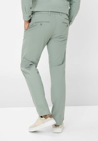 Mintgrüne Hose im Slim-Fit mit zwei Gesäßtaschen und Knopfverschluss sowie einer Bügelfalte, kombiniert mit weißen Sneakers.