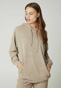 Felpa beige realizzata in tessuto morbido con finitura texturizzata, dotata di tasca frontale, cappuccio regolabile con cordino e vestibilità comoda.