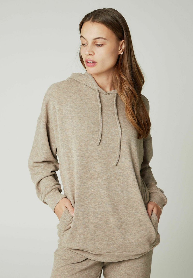 Felpa beige realizzata in tessuto morbido con finitura texturizzata, dotata di tasca frontale, cappuccio regolabile con cordino e vestibilità comoda.