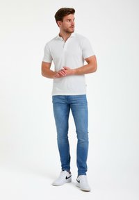 Polo blanco de manga corta con cuello y tres botones, combinado con jeans ajustados de color azul claro y zapatillas blancas. Diseño minimalista.