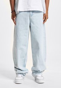 Lyseblå vide jeans laget av denim, med avslappet passform, rullede mansjetter og sømdetaljer, kombinert med hvite joggesko.