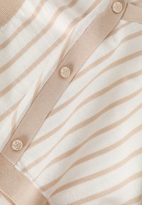 Top en tricot rayé crème et beige clair, avec une patte de boutonnage comportant des boutons ronds estampillés du logo et une finition en tissu texturé.