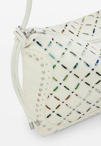 Borsa a mano in tessuto bianco con design a intaglio e dettagli colorati, componenti in argento e borchie. Chiusura con zip e manico elegante.