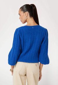 Maglione blu con texture e maniche a sbuffo, dotato di scollatura rotonda e sottile motivo a righe. Sul retro presenta un dettaglio con logo vicino al colletto.