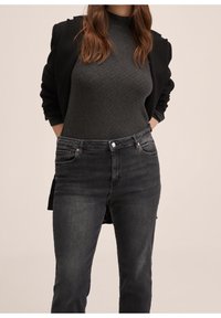 Blazer noir sur un haut gris foncé texturé, associé à un jean slim foncé avec poches avant et fermeture par bouton.