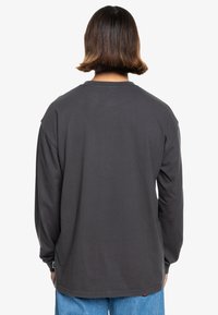 Long-sleeve gray cotton t-shirt with a relaxed fit, round neckline, and minimal stitching details, worn with light blue jeans.