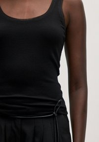 Zwarte geribbelde tanktop met een aansluitend ontwerp. Heeft een subtiele mesh halslijn en een verstelbare trekkoord aan de onderkant. Soepele textuur en minimalistische stijl.