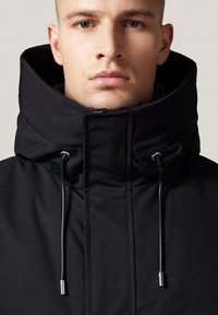 Czarna kurtka z kapturem, z wysokim kołnierzem, regulacją na sznurki i gładką teksturą. Detale w postaci przeszyć i metalowych akcentów.
