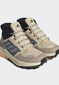 Zapatos de senderismo beige y negros con malla texturizada, suelas de goma, punteras reforzadas y acentos reflectantes; diseñados para condiciones impermeables.