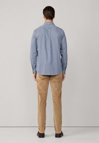 Camisa de franela a cuadros azules y blancos con cuello, puños abotonados, combinada con pantalones de corte en color beige claro y zapatos oscuros.
