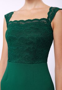 Grön klänning med spetsöverdel med blommönster och en figursydd, enfärgad grön kjol. Texturerad bodice och slätt tyg nedanför.