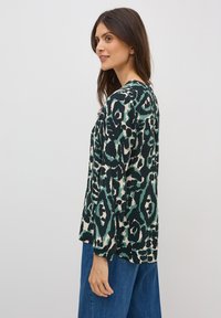 Blouse à manches longues avec un motif animal abstrait vert et noir, dotée d'une coupe décontractée et d'un col rond, associée à un pantalon en denim.