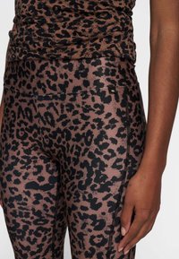Leggings con estampado de leopardo en marrón y negro; tejido suave y elástico; presentan costura lateral y una pequeña etiqueta de marca en la cintura.