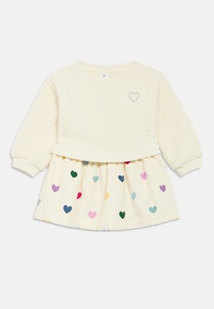 Krēmkrāsas džemperis ar teksturētu vilnas korpusu, sirds izšuvumu un krēmkrāsas svārki, rotāti ar krāsainiem sirds rakstiem dažādu izmēru.