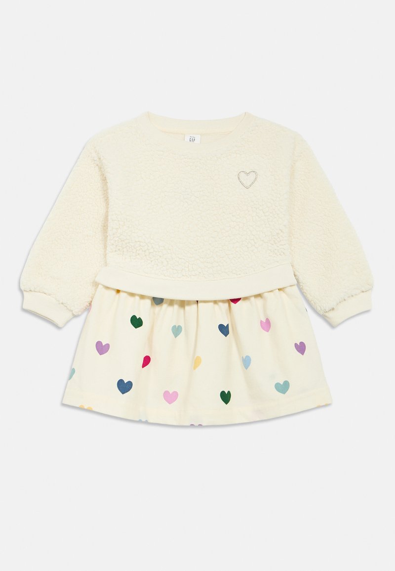 Krém színű pulóver texturált puha anyagú törzzsel, szív hímzéssel és krém szoknyával, amelyet különböző méretű, színes szívminták díszítenek.