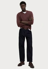Vínově červený svetr s výstřihem do V kombinovaný s námořnicky modrými kalhotami. Oblečení doplňuje hnědý pásek a šněrovací boty. Látka vypadá hladká a strukturovaná.