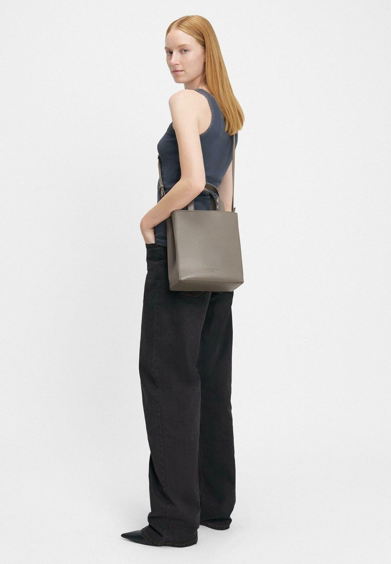 Szara skórzana torebka o usztywnionym kwadratowym kształcie, z krótkimi uchwytami u góry oraz długim regulowanym paskiem. Noszona w sposób casualowy przy ciemnym stroju.