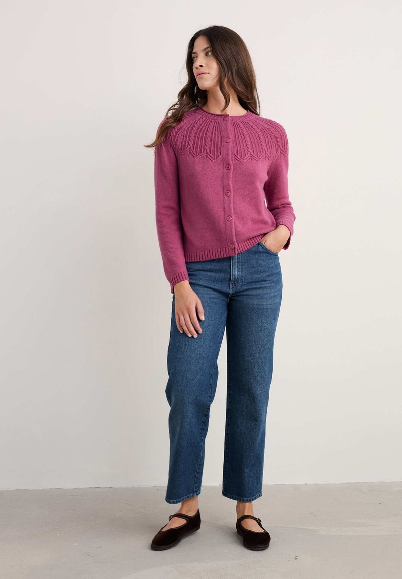 Cárdigan magenta con patrón texturizado de hojas en el canesú, seis botones, puños y dobladillo acanalados. Combinado con jeans de pierna recta azul.