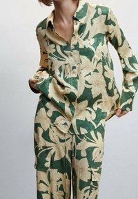 Ensemble de chemise et pantalon à motifs floraux verts et beige, fabriqué en tissu léger ; comprend une chemise à col et un pantalon ample.