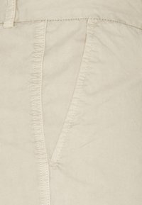 Pantaloni beige in cotone con una texture liscia, dotati di tasche laterali e cuciture visibili lungo le cuciture.