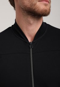 Must Black zip-up jacket with a high collar, featuring a sleek finish and contrasting zip. Smooth texture and minimalistic design.