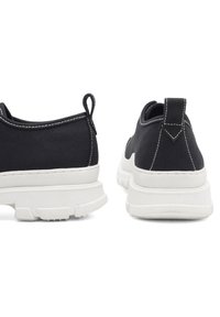 Czarne płócienne trampki z białymi gumowymi podeszwami, z pętlą do wciągania z tyłu oraz kontrastującymi białymi przeszyciami wzdłuż szwów.
