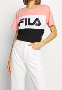Färgblock t-shirt med rosa, vit och svart sektioner. Stort "FILA"-logotyp i svart och rött. Korta ärmar, avslappnad passform.