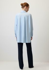 Gaiši zils pogājams krekls no gludas auduma ar garām piedurknēm un klasisku apkakli, kombinēts ar taisnām melnām biksēm.