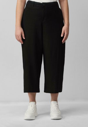 Black cropped pants with a loose fit, featuring a single button closure and subtle texture. Paired with white sneakers for contrast.