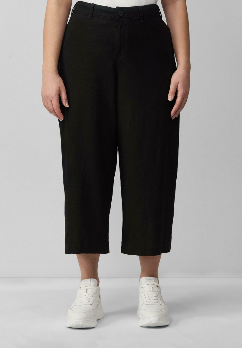 Zwarte cropped broeken met een losse pasvorm, voorzien van een enkele knoopsluiting en een subtiele textuur. Gekoppeld met witte sneakers voor contrast.