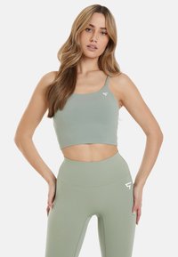 Lys grøn sport crop top med tynde stropper og et logo. Båret med matchende højtaljede leggings med en sømløs design.