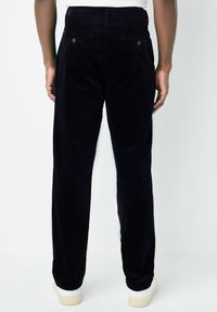 Navy corduroy trousers with a straight cut, featuring two back pockets and subtle ribbing texture. Paired with light, casual footwear.