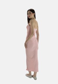 Rosa, eng anliegendes Maxikleid mit dünnen Trägern, knielangem Schlitz und elastischem Stoff. Getragen mit flachen, verzierten grauen Schuhen.