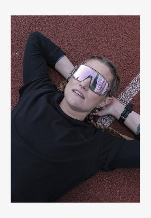 Sunglasses with large mirrored lenses, black round frame, and a reflective gray tint. Black shirt worn on a textured red athletic surface.