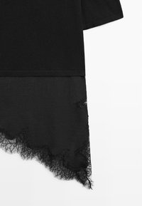 Haut noir à manches courtes avec un ourlet asymétrique orné d'une bordure en dentelle noire qui dépasse du tissu principal.