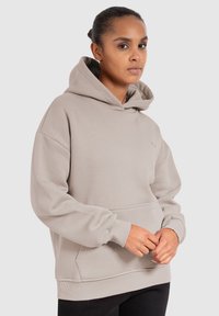 Hoodie beige clair en tissu doux. Doté d'une poche frontale, de poignets côtelés et d'une grande capuche. Design simple et décontracté avec un branding minimal.