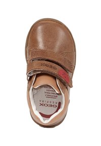 Scarpa in pelle marrone con cinturino in velcro, punta arrotondata e fodera interna imbottita. Presenta un accento rosso vicino al cinturino. Suola morbida.