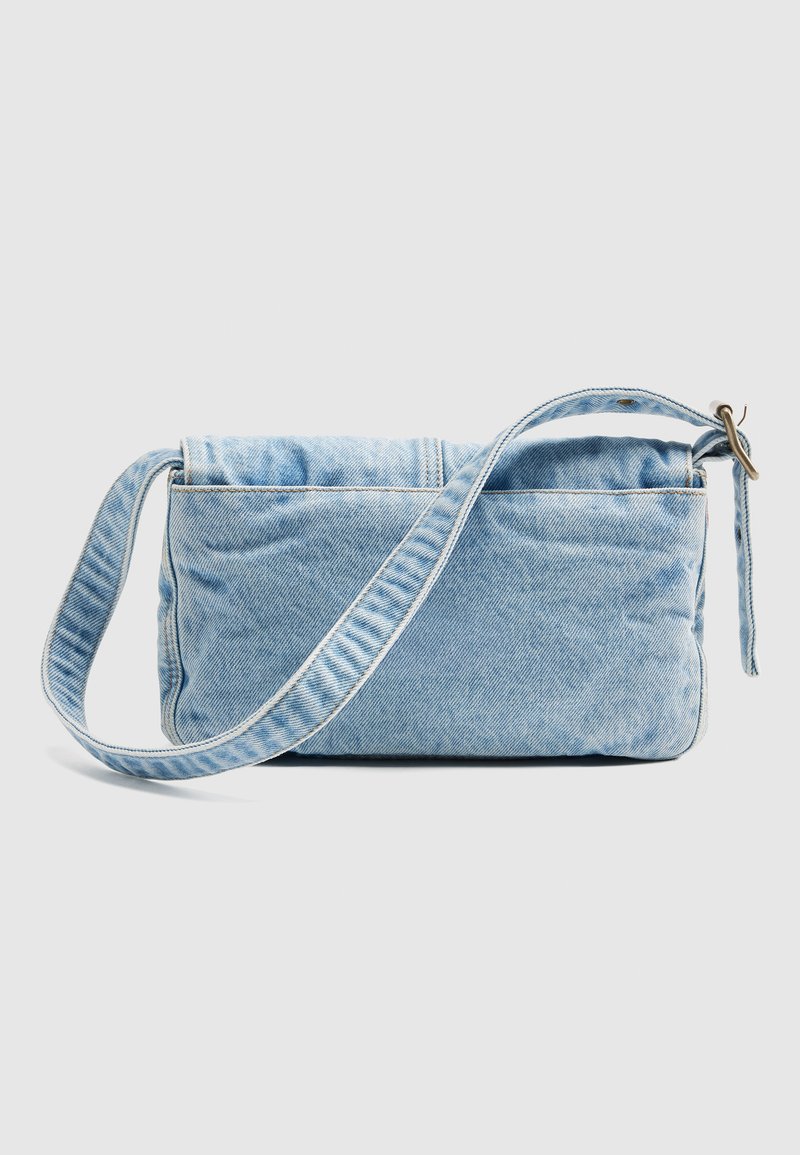 Borsa a tracolla in denim azzurro chiaro con tracolla regolabile e fibbia in ottone, mostrata su uno sfondo chiaro uniforme.