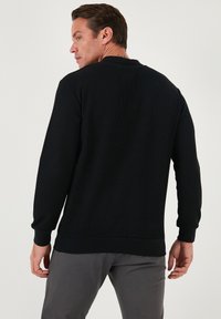 Sudadera negra acanalada con mangas largas y cuello redondo. Presenta una textura en la tela y un ajuste relajado, que se extiende por debajo de la cintura.