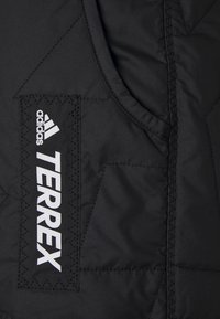 Svart quiltad jacka med "TERREX" och Adidas-logotyper i vitt, med en slät textur och vinklad sömnadsdetalj.