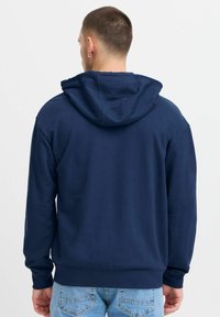 Marineblauwe hoodie met een trekkoordkap, ribgebreide manchetten en zoom. Gemaakt van een gestructureerde katoenstof, heeft het een relaxte pasvorm voor comfort.
