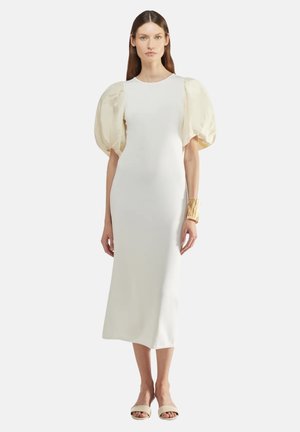 Witte midi-jurk met een getailleerde silhoët, voorzien van grote crèmekleurige pofmouwen. De jurk heeft een gladde textuur, aanv complemented met een gouden manchetketting en neutrale sandalen.