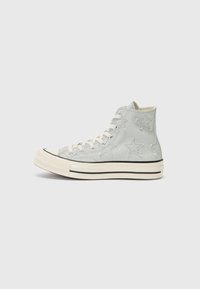 Heledad sneakerid heledates hallidest hallilõngast, millel on tikitud tähekad, valged paelad ja beezist kummitald musta aktsentliiniga.