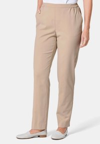 Pantalons beiges à taille élastique avec un design à jambes droites, dotés de poches latérales. Texture lisse et coupe taille intermédiaire, associés à des chaussures blanches à enfiler.