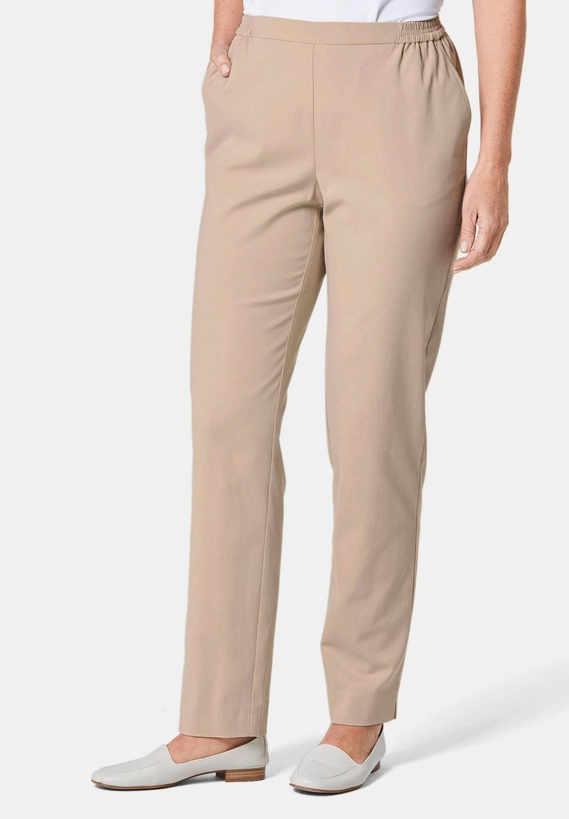 Pantalons beiges à taille élastique avec un design à jambes droites, dotés de poches latérales. Texture lisse et coupe taille intermédiaire, associés à des chaussures blanches à enfiler.