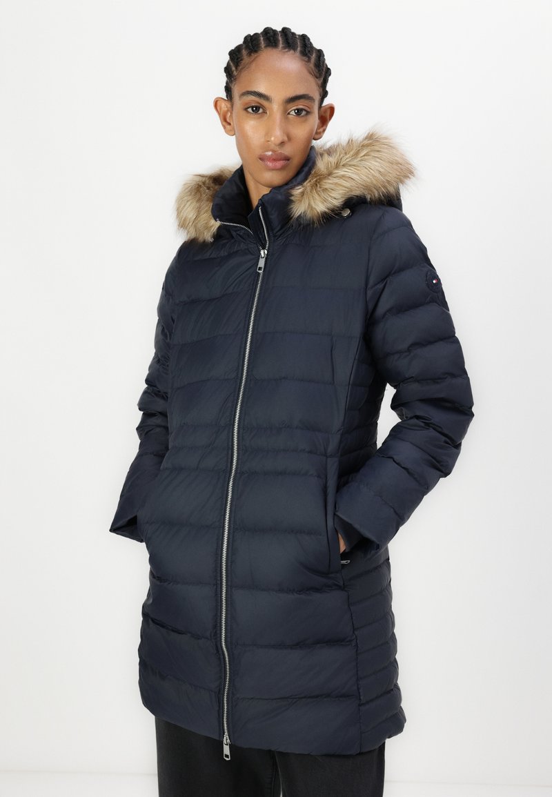 Marineblauer Puffer-Mantel mit Kunstfellbesatz an der Kapuze, Reißverschluss, gestepptem Design, langen Ärmeln und Seitentaschen. Schlichte, legere Gestaltung.