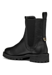 Botín negro de cuero hasta el tobillo con paneles elásticos en los costados, punta redondeada y suela de goma texturizada. Presenta un acento metálico circular en el talón.